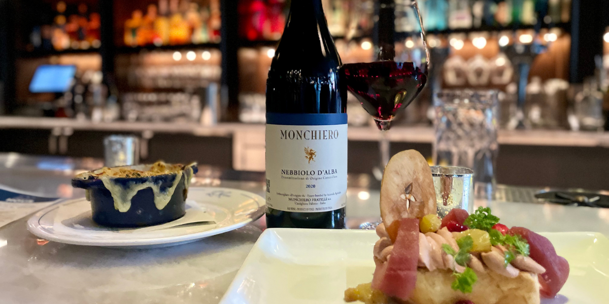 When Fall envelopes the rolling hills of Italy’s Piedmont region, the fog, or ‘nebbia’ that gives the Nebbiolo grape variety its name, floats through the vineyards, cooling the grapes before harvest. This thick-skinned grape produces some of Italy’s finest wines, such as Barolo and Barbaresco. In downtown Denver, this approachable example offers all the flavors and structure we love in this Autumn classic without needing hours of decanting or years of aging in the bottle.
Nestled in the heart of the famed Barolo region in Castiglione Falletto, the Monchiero family has been making remarkable red wines from Nebbiolo since the 1950s. Starting as a grape grower, the family started producing their premium wines in the 70s. The Nebbiolo d’Alba gushes with layered berry flavors and classic notes of violets. Paired with Bistro LeRoux’s classically delicious French Onion Soup and a plate of Foie Gras with Chicken Liver Mousse, the wine offers a pop of tart fruit like a garnish of dried cranberry or cherry. Each of these rich menu items strikes a balance in concert with the wine that screams Fall.