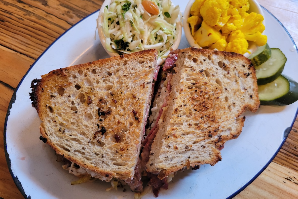 white plate with rye bread sandwich and deli sides