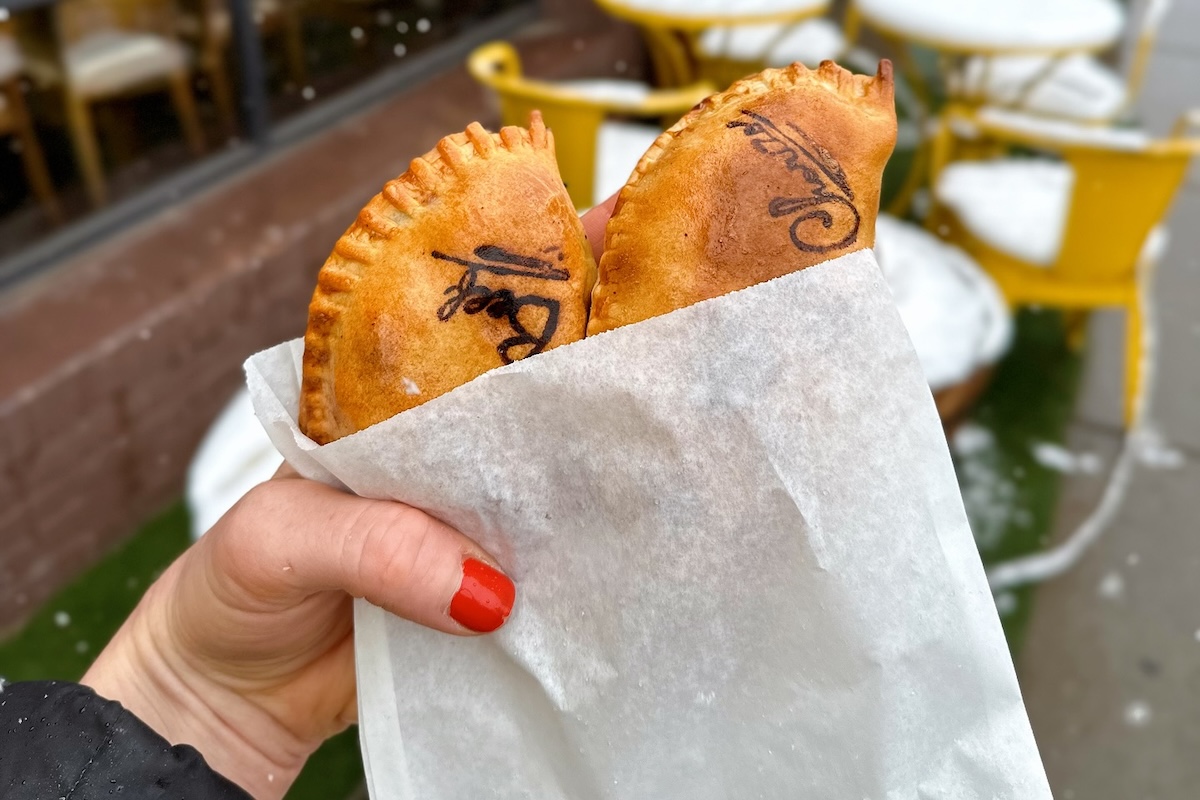 hand holding empanadas in a paper bag