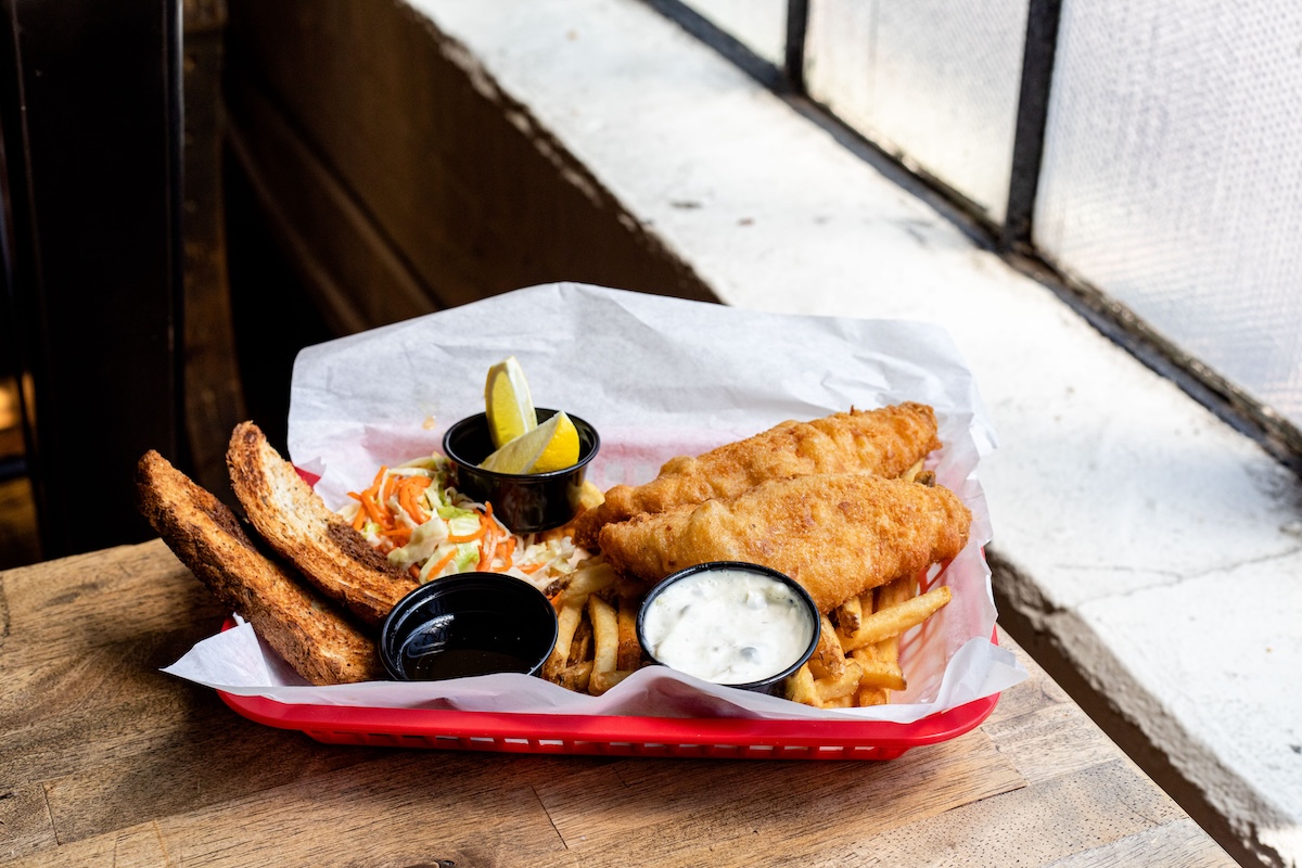 wood table by window with a basket of fish and chips on it