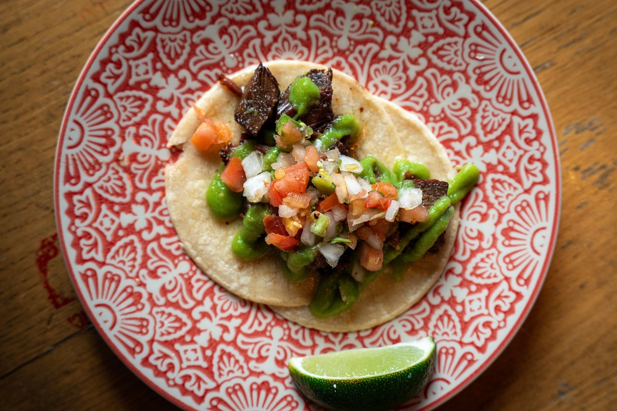 Kachina_Cantina_Taco A taco from Kachina Cantina sits on a red and white patterned plate, topped with grilled meat, green sauce, pico de gallo, and served with a lime wedge.