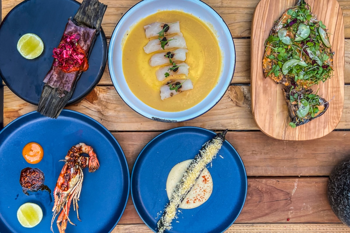 La_Diabla_Patio_Menu An overhead view of La Diabla’s patio table set with vibrant dishes, including grilled shrimp, tamal, esquites, ceviche, elote, and a roasted veggie entrée.