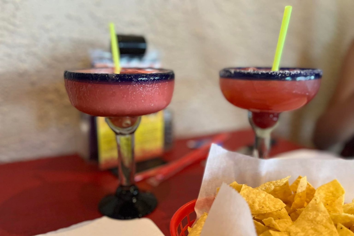 Los-Arcos_photo courtesy of Brittany-Anas Two frozen strawberry margaritas in salt-rimmed glasses with yellow straws sit on a red table next to a basket of tortilla chips at Los Arcos restaurant.