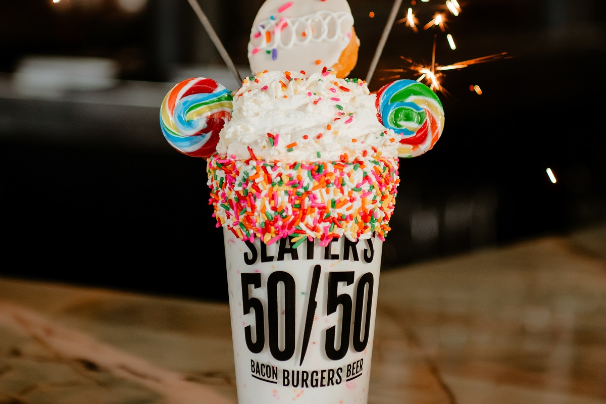 Slaters 50_50_Happy Happy Birthday Shake_photo courtesy of Slaters 50_50 Over-the-top birthday milkshake topped with whipped cream, rainbow sprinkles, lollipops, a donut, and sparklers, served in a Slater’s 50/50 cup.