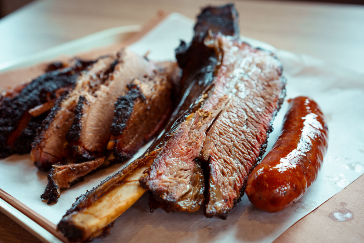 Close-up of a BBQ tray from Best Barbecue Spots Around Denver with sliced brisket, beef rib, and sausage on butcher paper, glistening with juices.