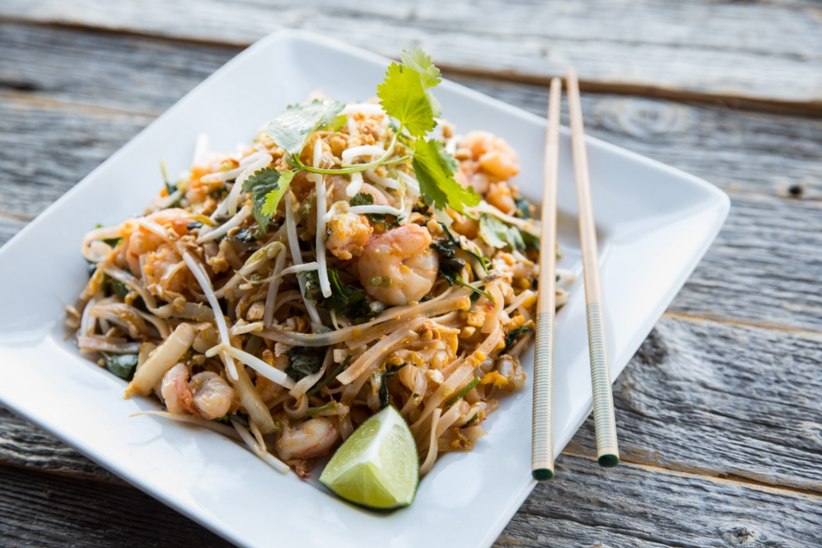 big bowl Big Bowl shrimp pad Thai with noodles, bean sprouts, cilantro, peanuts, and lime wedge, served on a white square plate with chopsticks on the side.