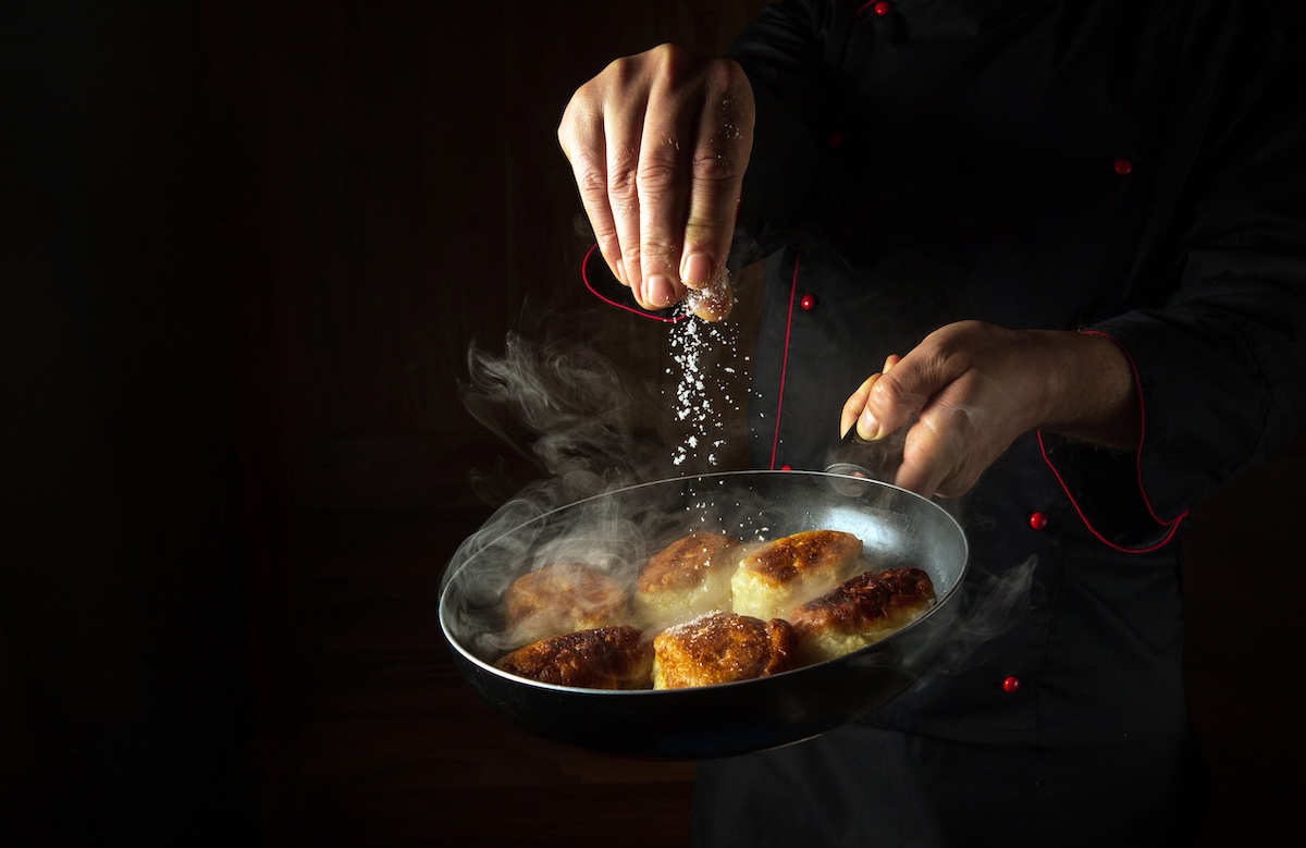 The chef salts hot pancakes in a frying pan while frying Concept of cooking blini in a restaurant kitchen