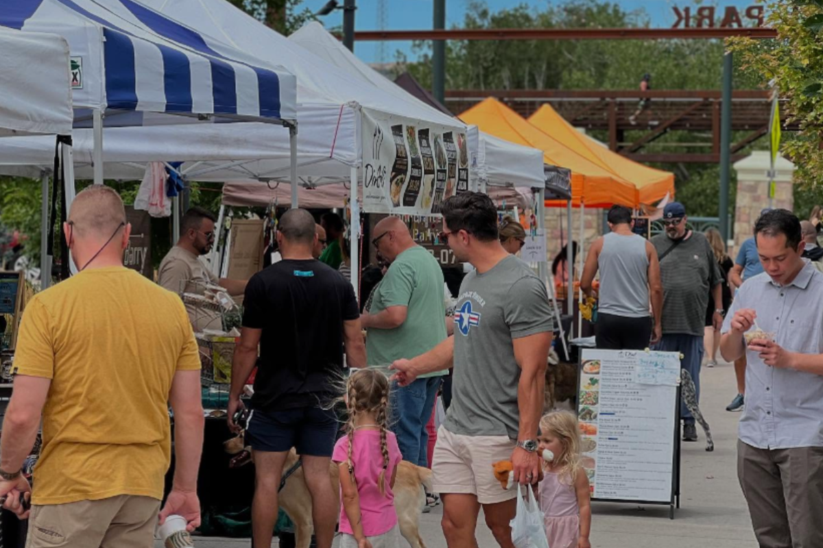 festival park farmers market castle rock People walk with kids and shop at Festival Park Farmers Market in Castle Rock, surrounded by vendor tents with food, drinks, and handmade goods on display.