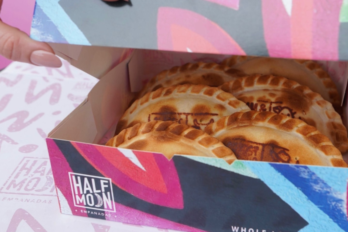 half moon empanadas A close-up of a colorful box filled with golden-brown Half Moon empanadas, each stamped with a logo and packed neatly inside.