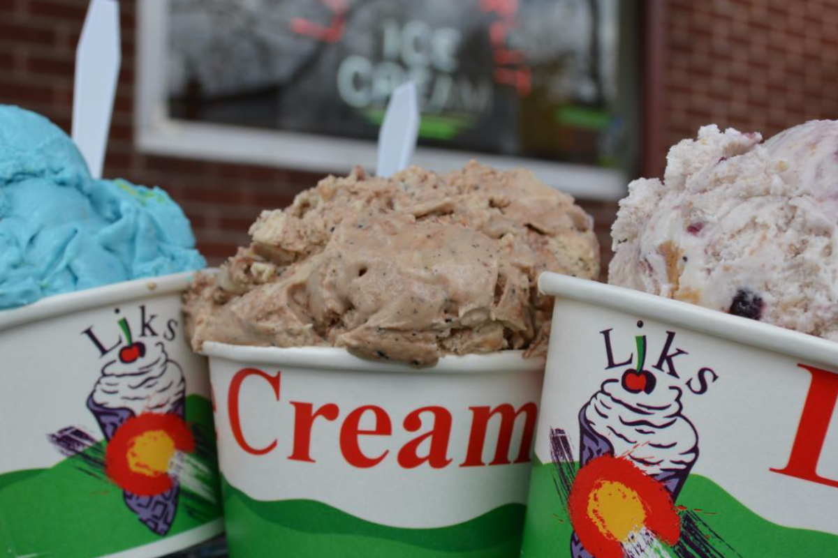 liks ice cream Close-up of three colorful ice cream scoops in Liks ice cream cups, featuring blue, chocolate, and berry flavors, with a shop window blurred in the background.