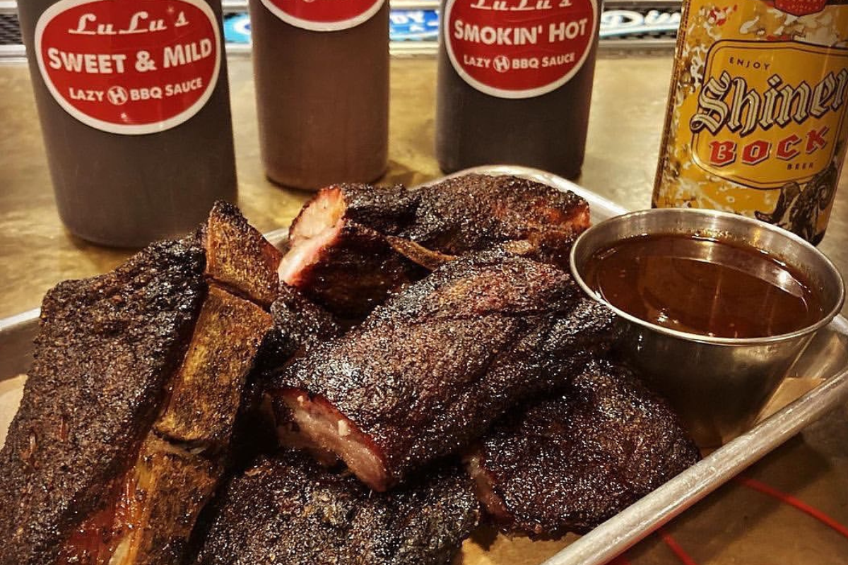 lulus bbq Tray of bark-crusted ribs from LuLu’s BBQ, served with a cup of barbecue sauce, Shiner Bock beer, and bottles of house-made sweet and spicy sauces.