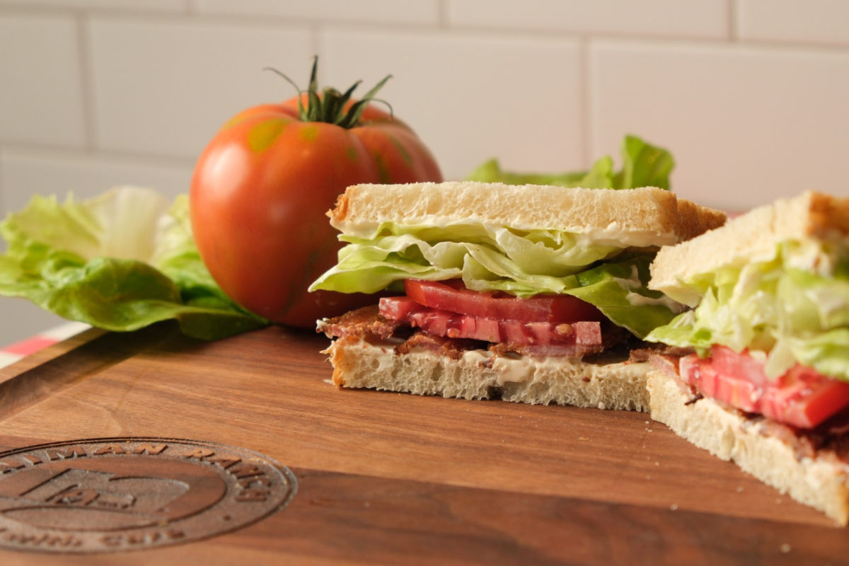 marczyk fine foods Marczyk Fine Foods BLT sandwich stacked with fresh lettuce, ripe tomato, crispy bacon, and mayo on sliced white bread, served on a wooden cutting board.