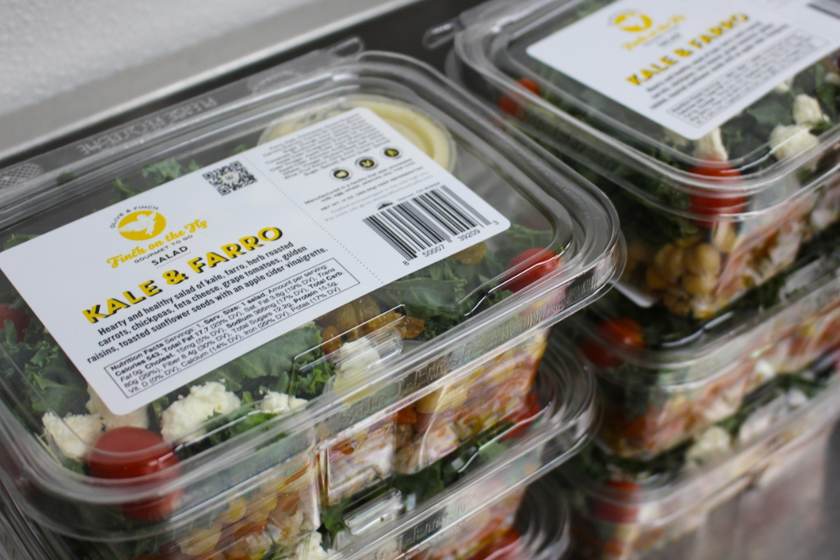 olive finch on the fly Stacked containers of Olive & Finch’s Kale & Farro salad, filled with greens, chickpeas, tomatoes, feta, and vinaigrette, labeled “Fresh on the Fly.”