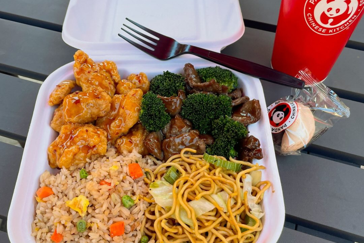 panda express A Panda Express combo meal with orange chicken, beef with broccoli, fried rice, chow mein, fortune cookie, and a drink in a red cup on a gray table.