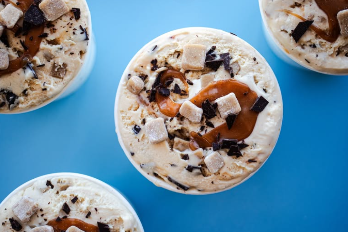 sadboy creamery Top view of Sadboy Creamery pints filled with caramel swirls, chocolate chunks, and cookie dough pieces, set against a bright blue background.