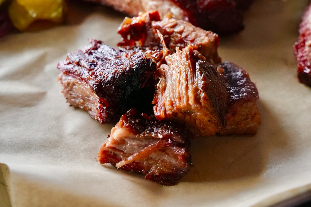seasoned swine bbq Close-up of burnt ends and ribs from Seasoned Swine BBQ, served on butcher paper with pickles, onions, and sides like mac and cheese and baked beans.