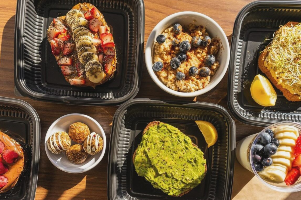 superfruit republic Superfruit Republic breakfast spread with avocado toast, oatmeal with blueberries, fruit-topped toast, yogurt parfait, and energy bites in black containers.