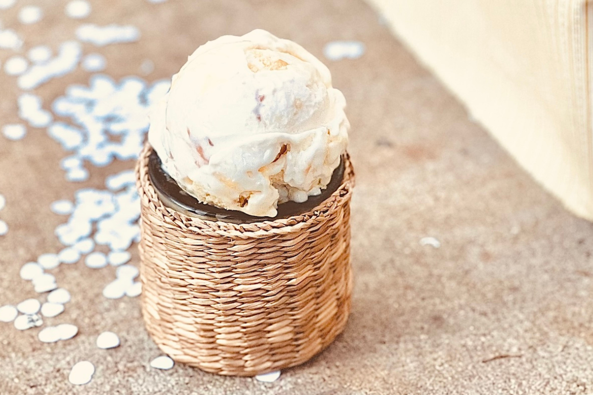 sweet action ice cream Single scoop of small-batch ice cream displayed in a woven holder on a neutral background, highlighting handcrafted texture and creamy swirl.