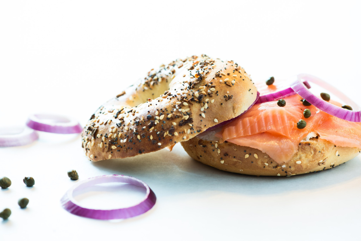 the bagel deli An everything bagel sandwich with smoked salmon, red onion rings, and capers on a white surface, with extra onion slices and capers scattered around.