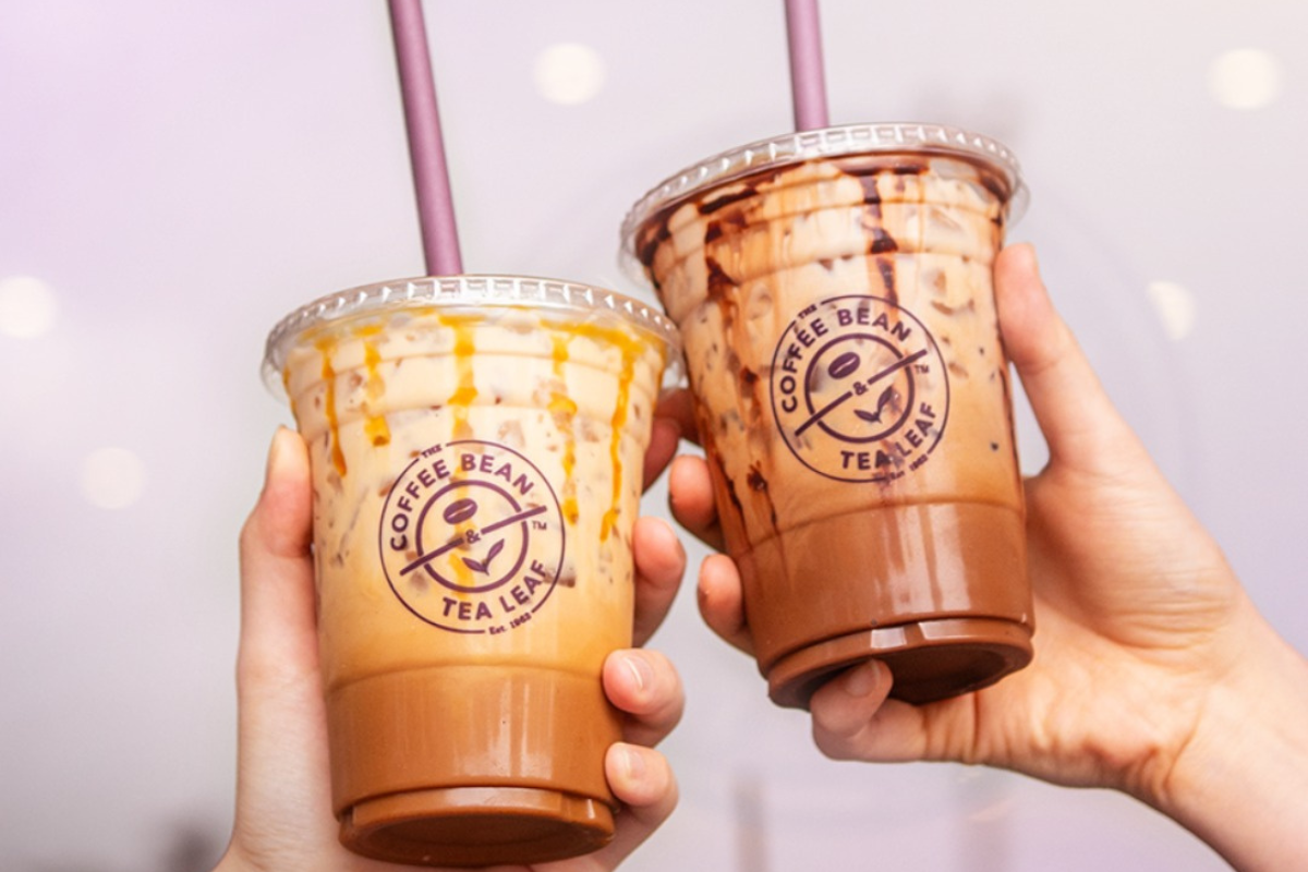 the coffee bean tea leaf Two iced drinks from The Coffee Bean & Tea Leaf held up, one with caramel drizzle and the other with chocolate drizzle, both in branded plastic cups.