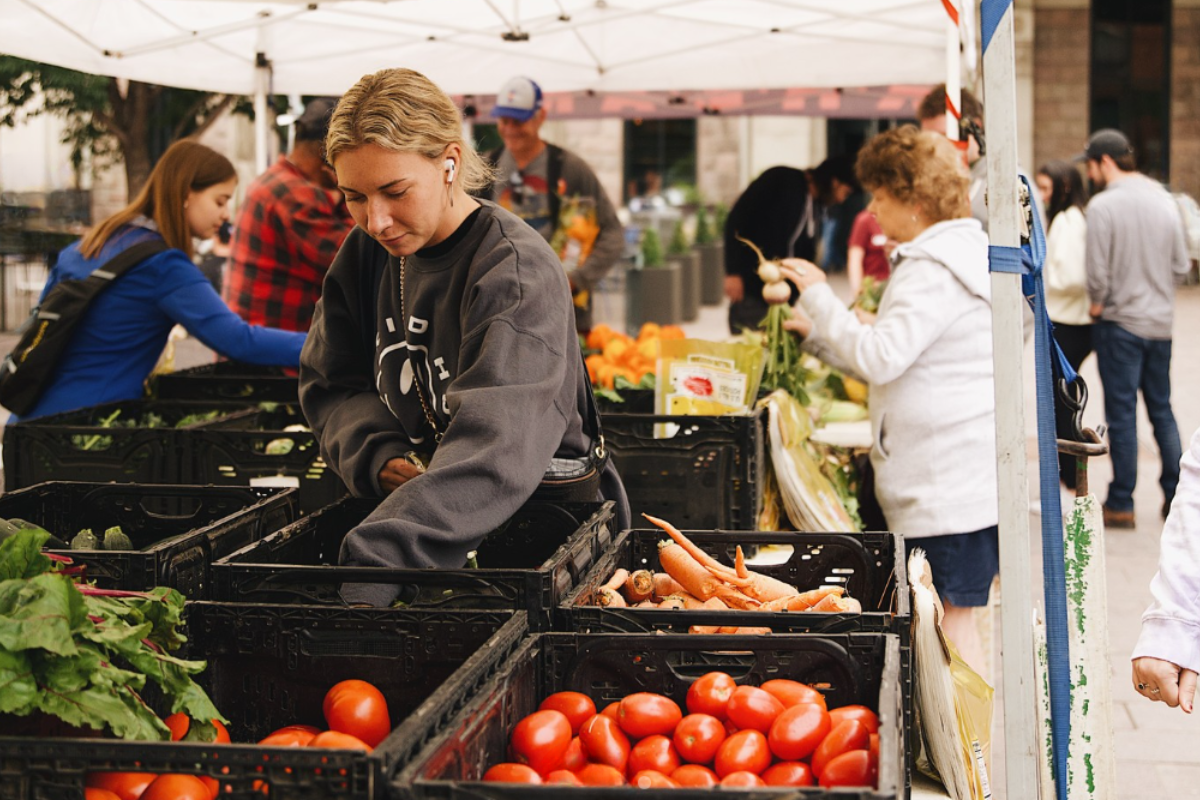 union station urban market Shoppers at Union Station Urban Market in downtown Denver browse crates filled with fresh tomatoes, carrots, and leafy greens under a white canopy tent.