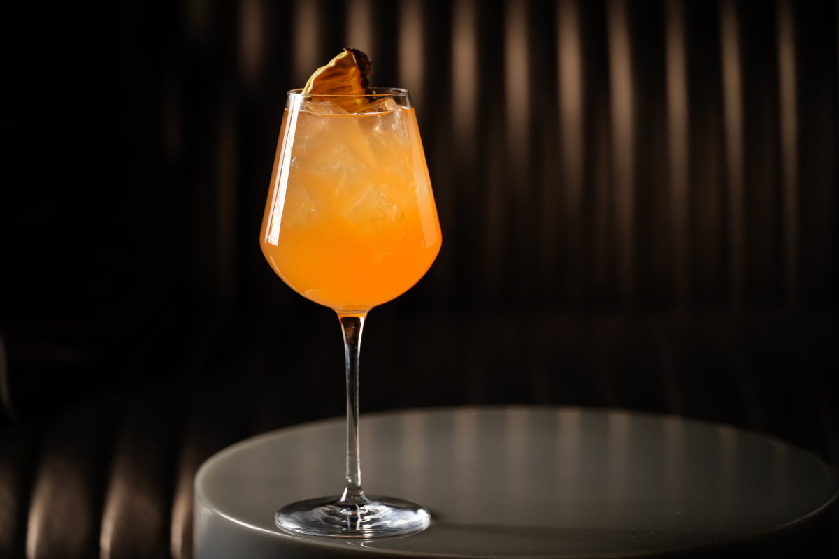 Sunset Spritz cocktail with rum, Aperol, and pineapple shrub, served over ice in a wine glass on a round table at Halo rooftop bar in Denver.