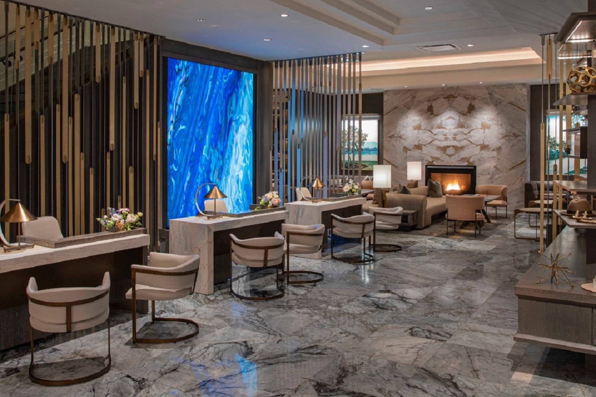 Hotel Clio Hotel Clio’s lobby in Denver featuring marble floors, a glowing blue art wall, fireplace seating, and modern desks with gold-accented lighting.
