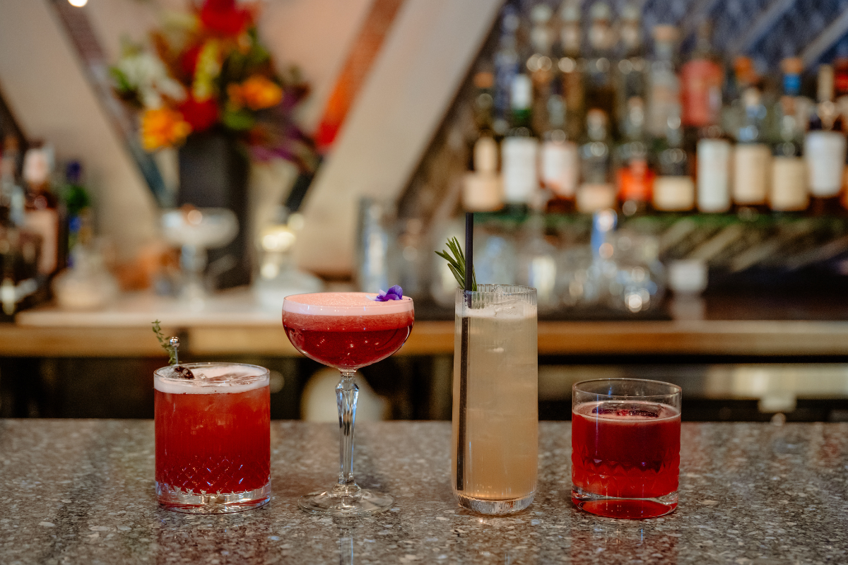 Four colorful zero-proof spritz cocktails garnished with herbs and flowers, lined up on a marble bar counter at Nocturne jazz and supper club in Denver.