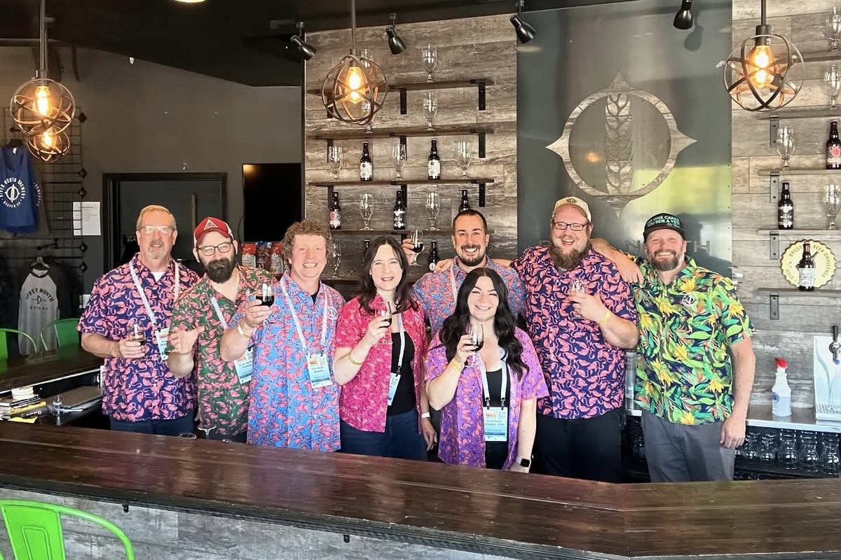 River_North_Brewery River North Brewery staff and brewers in colorful shirts smiling behind the bar, holding beer samples during a brewery event or beer festival in Denver.