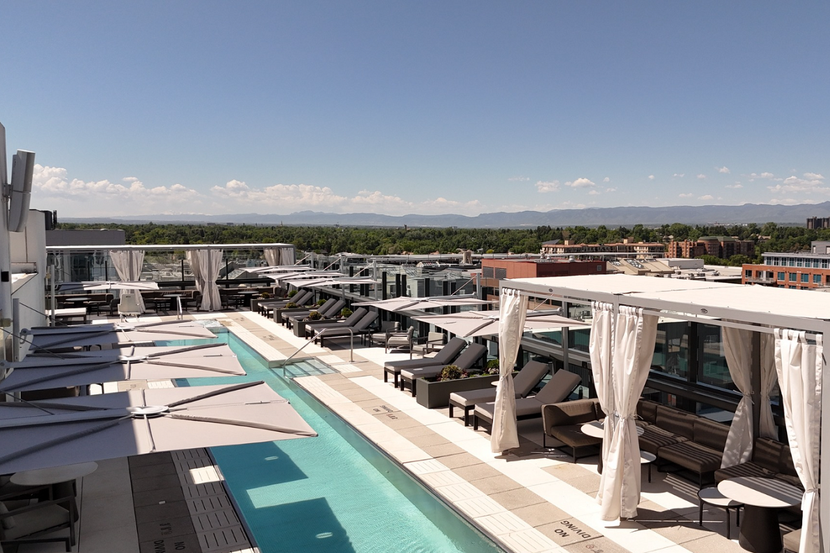 The Jacquard Rooftop pool deck at The Jacquard in Denver, with lounge chairs, shaded cabanas, and mountain views on a clear day.