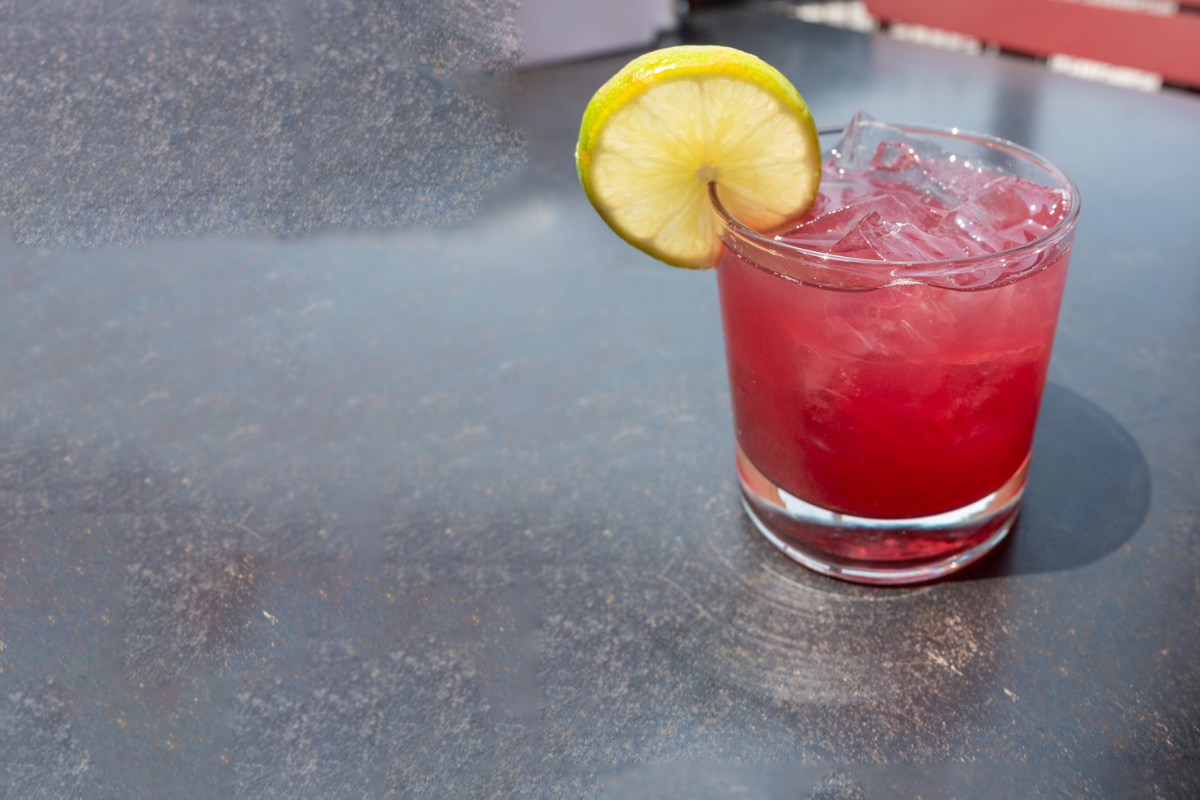 Watermelon Spritz from Atomic Cowboy, a pink cocktail served over ice in a short glass with a lemon wheel garnish, set on an outdoor tabletop.

