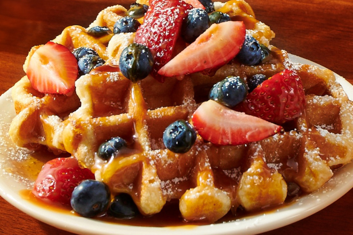 dennys Liège waffle topped with fresh strawberries, blueberries, powdered sugar, and caramel drizzle at Denny's in Denver.