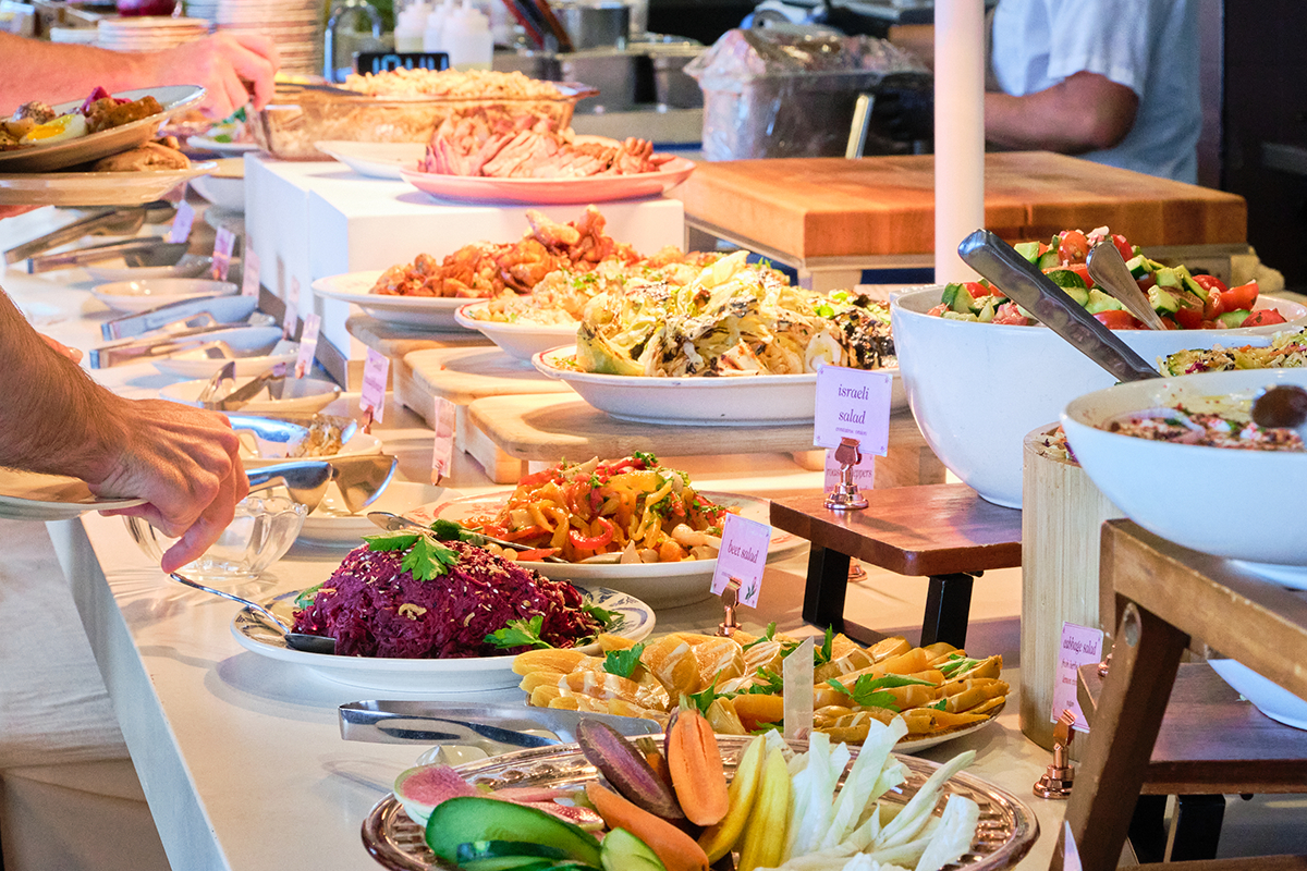saftas israeli brunch buffet Colorful Israeli brunch buffet with salads, grilled vegetables, fresh fruit, and shared dishes at Safta in Denver, with guests building their own plates.