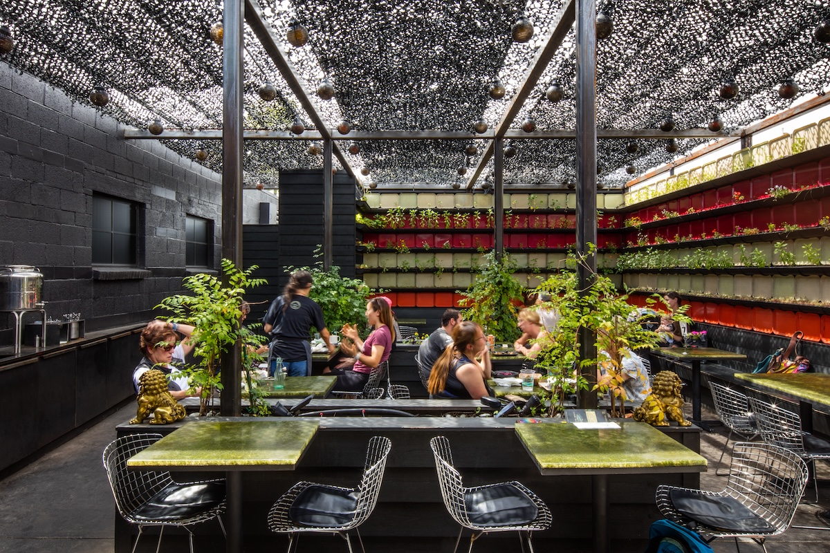 Guests dine under a netted canopy on the lush, plant-filled patio at Vital Root in Denver, surrounded by colorful vertical garden walls and greenery.