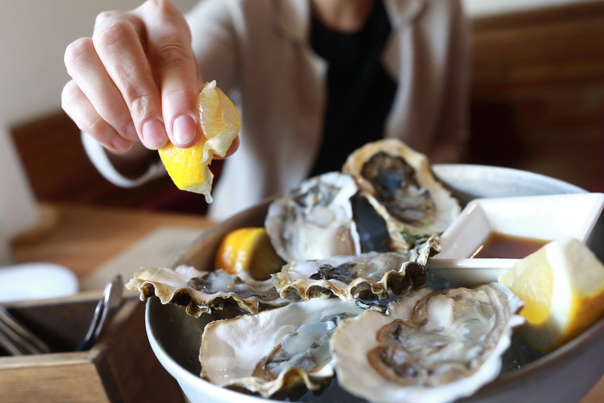 Woman sprinkles oysters with lemon juice in restaurant oysters with lemon on hand squeeze stock image